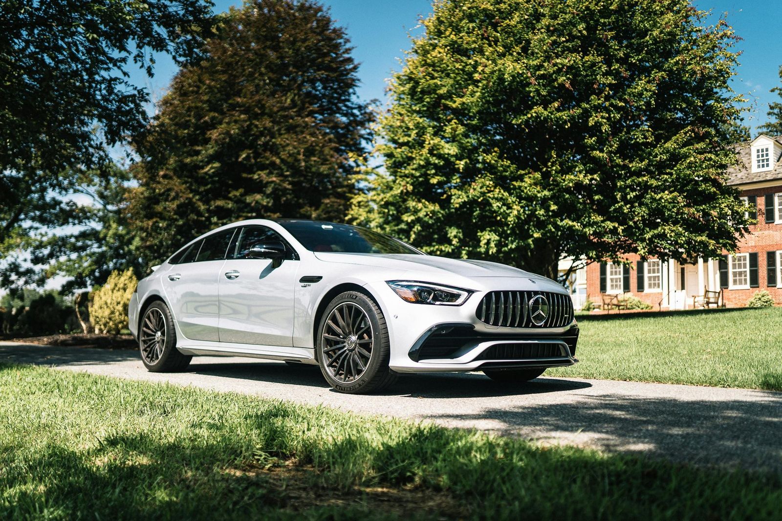 A white Mercedes sedan, washed and polished, parked on a driveway in front of a brick house