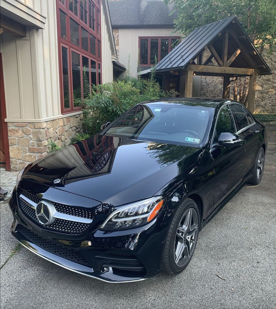A black Mercedes sedan after an exterior detail, gleaming in a driveway outside a house