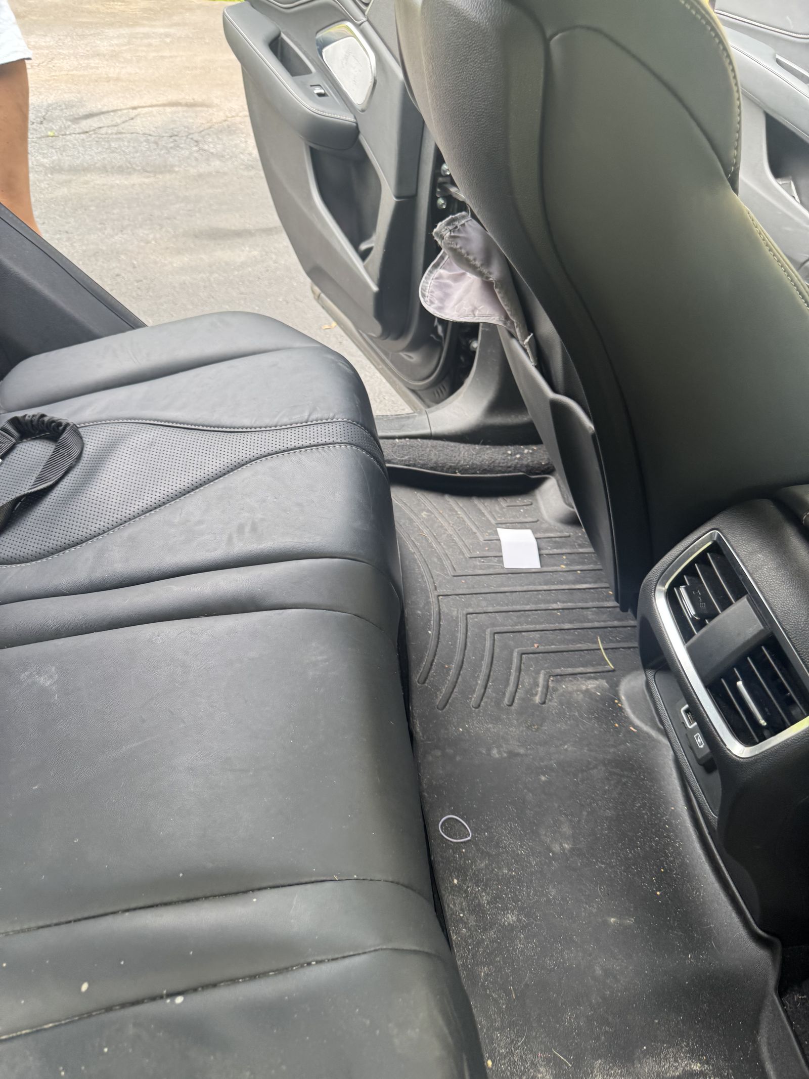 Rear seat of an SUV before an interior detail, with dirt and crumbs on the leather and the floor mat